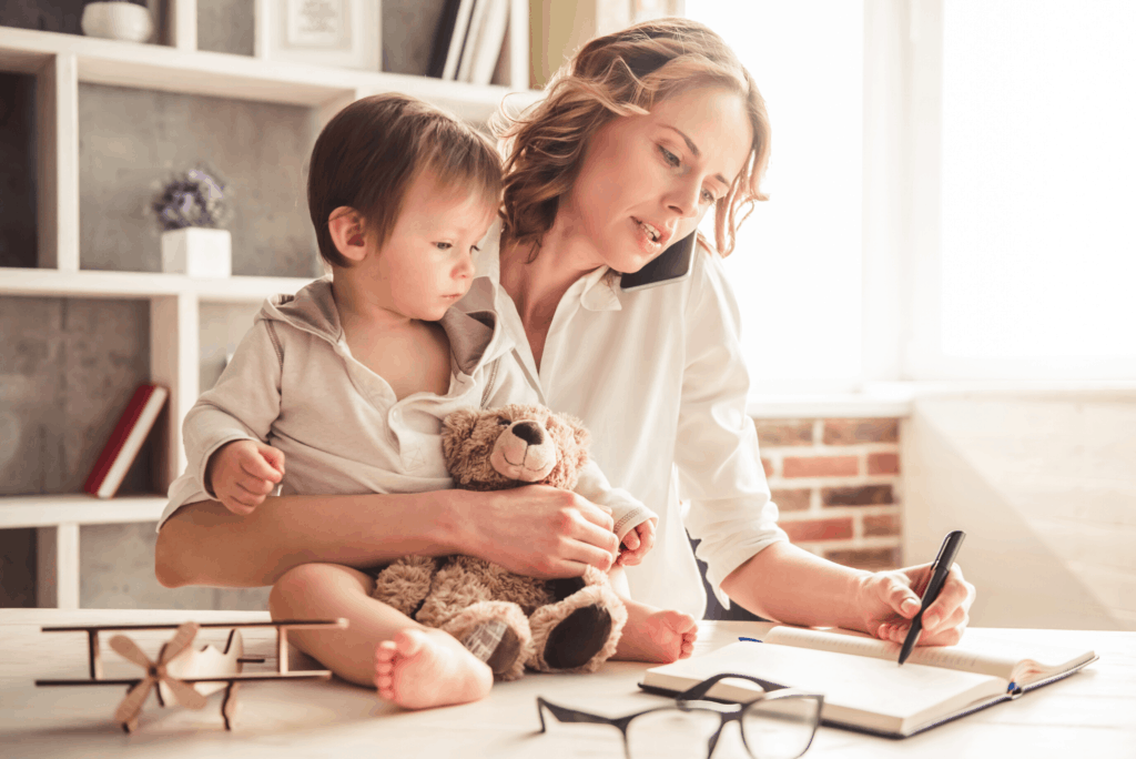 mother on phone while child sits on desk as she works