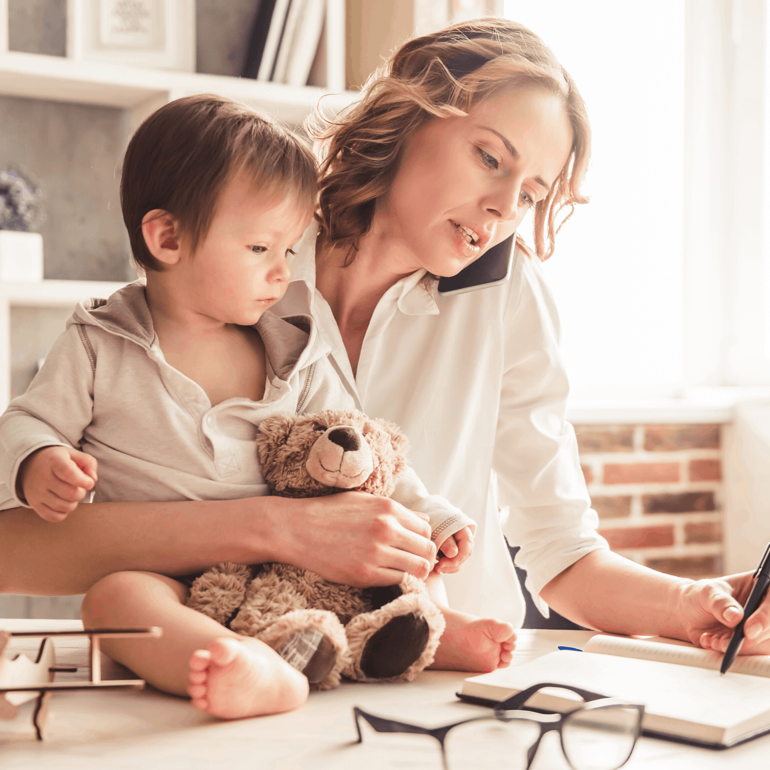 mother on phone while child sits on desk as she works