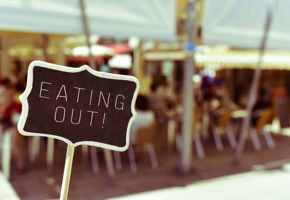 closeup of a chalkboard with the text eating out, in the busy terrace of a restaurant