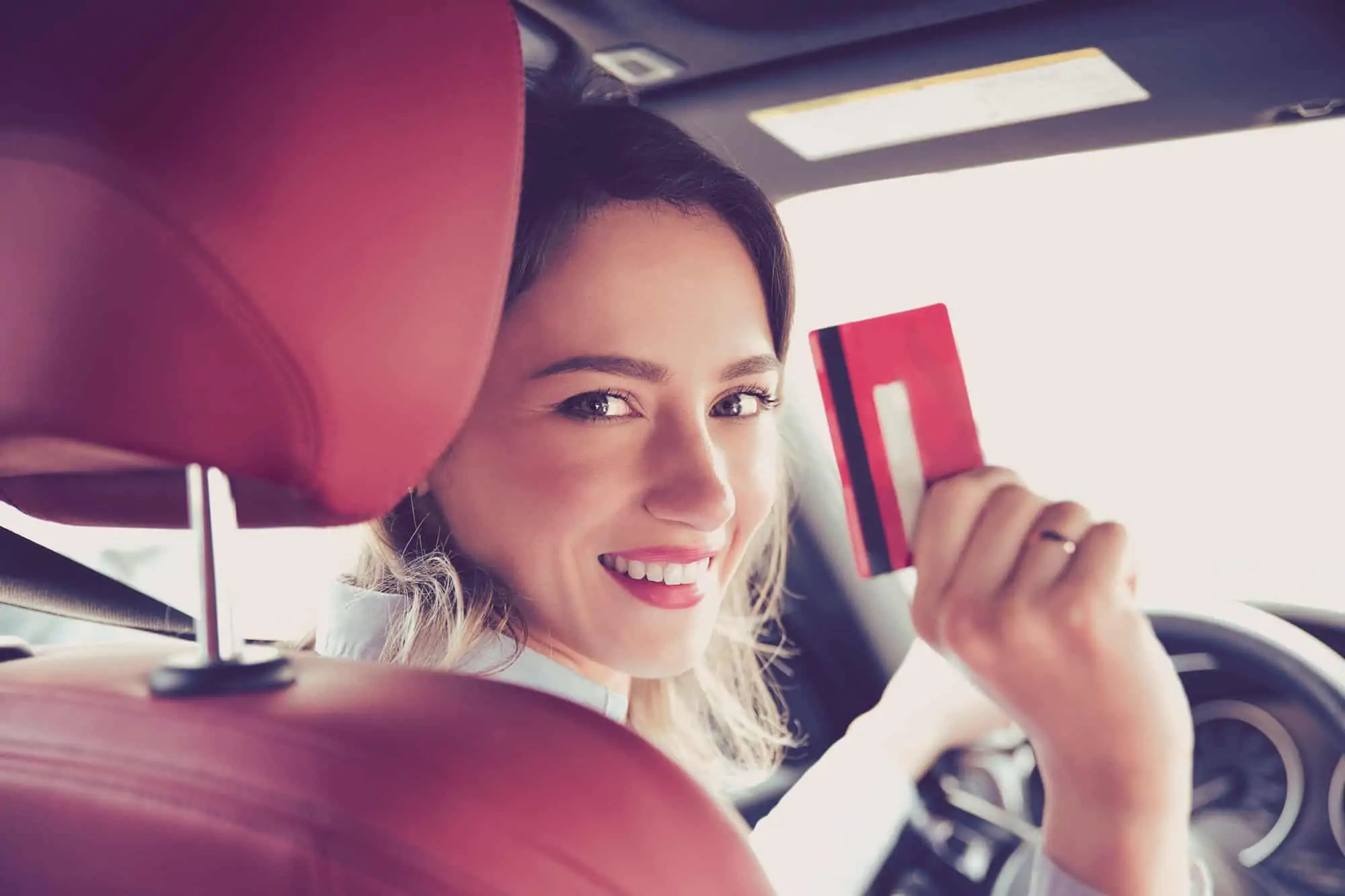 woman sitting in a car looking back over shoulder wiht credit card