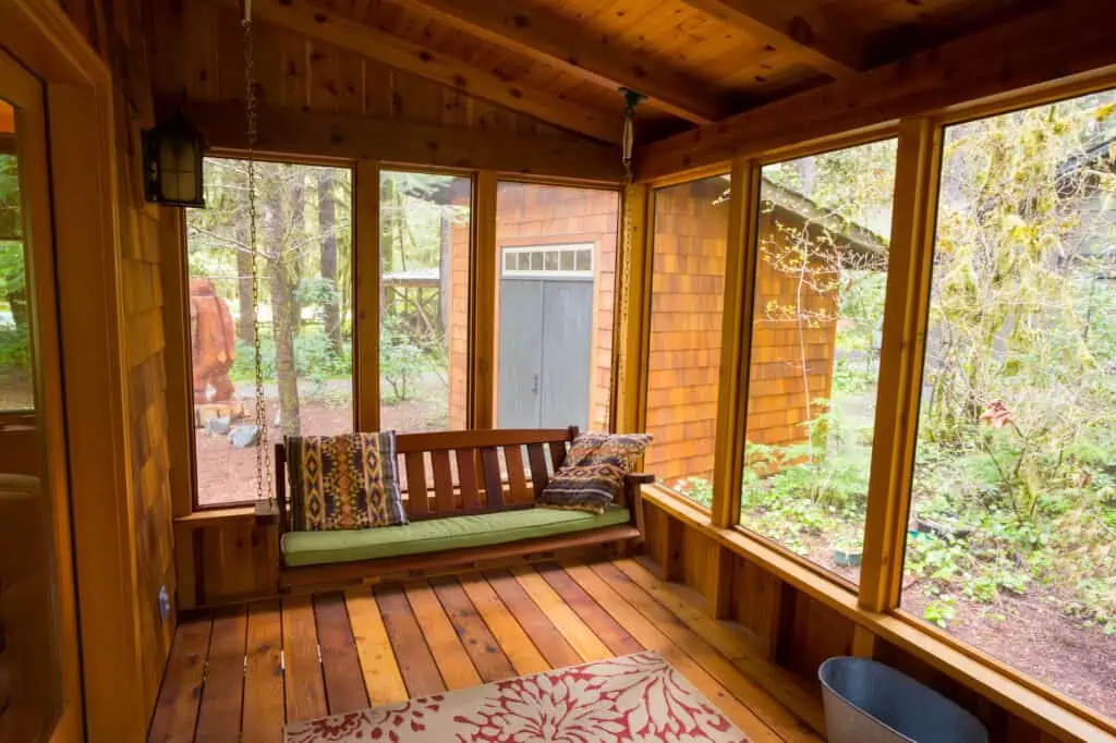 Bench swing hung by chain looking comfortable on a screened in porch.