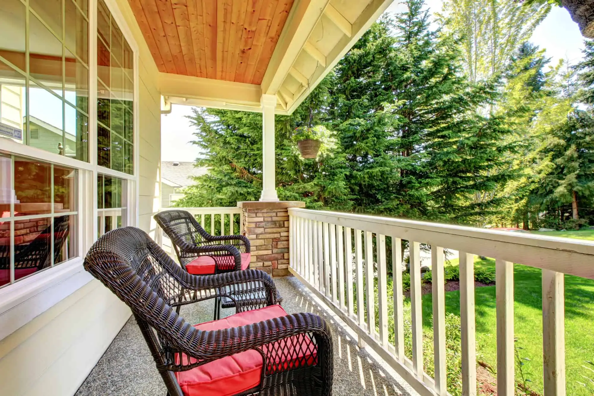 Front covered porch with brown chairs and red cushions.