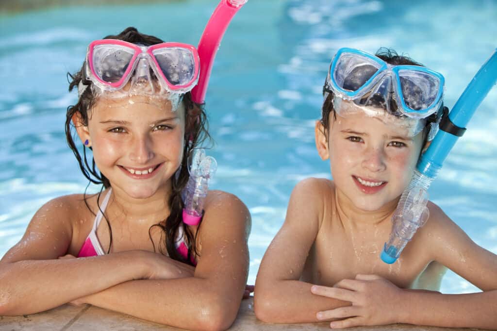 Happy young children, boy and girl, relaxing on the side of a swimming pool wearing blue and pink goggles and snorkel