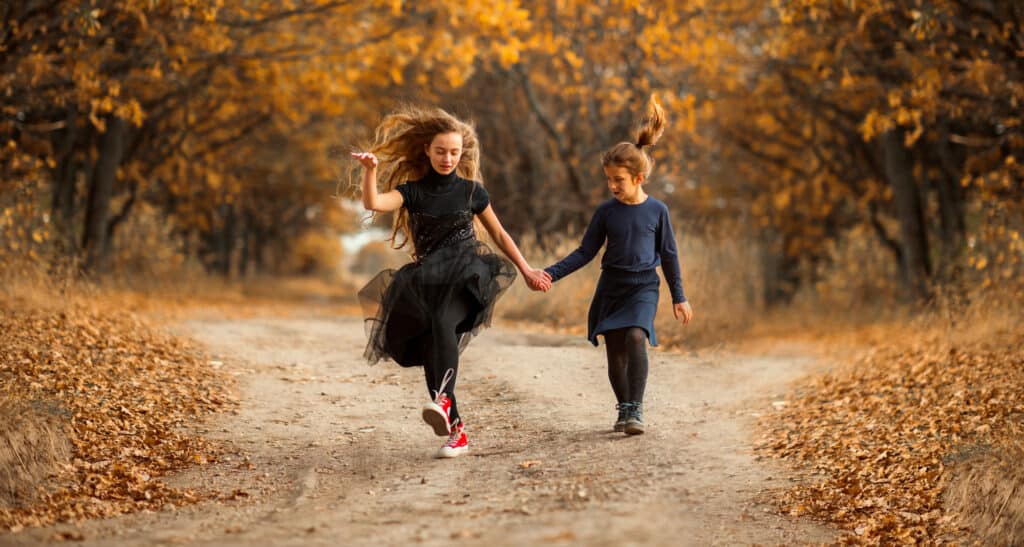 Two teenage girls walk along a forest road in the warm autumn. They are dressed in dark clothes. Halloween concept. The family concept. Friendship between sisters in the same family.