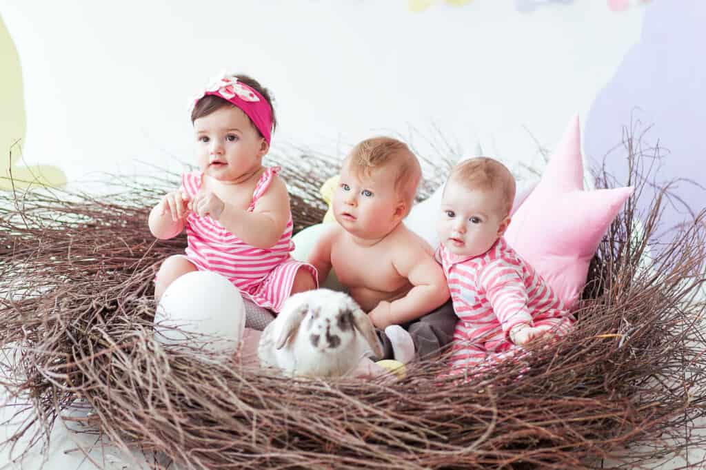 Happy Easter. Cute little baby girls and boy on Easter day. Kids hunting for Easter eggs in the handmade nest. Children having fun and playing with bunny.