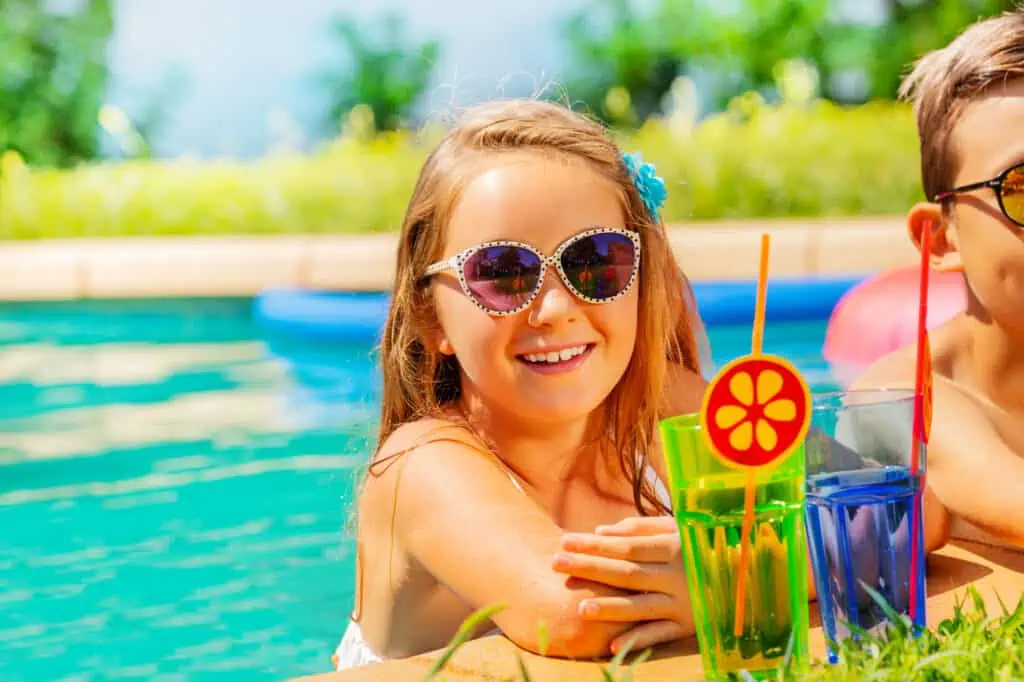 Portrait of smiling girl in sunglasses drinking refreshing beverage, having fun during pool party in summer