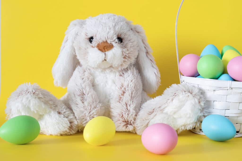 Easter stuffed bunny with colored eggs and easter basket on yellow background