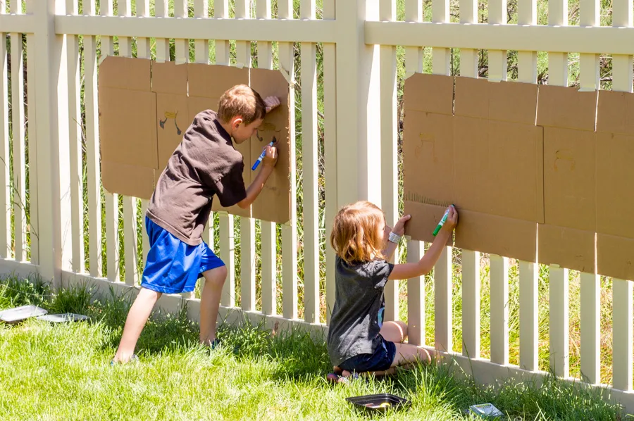 kids painting cardboard hung up outside on a fence