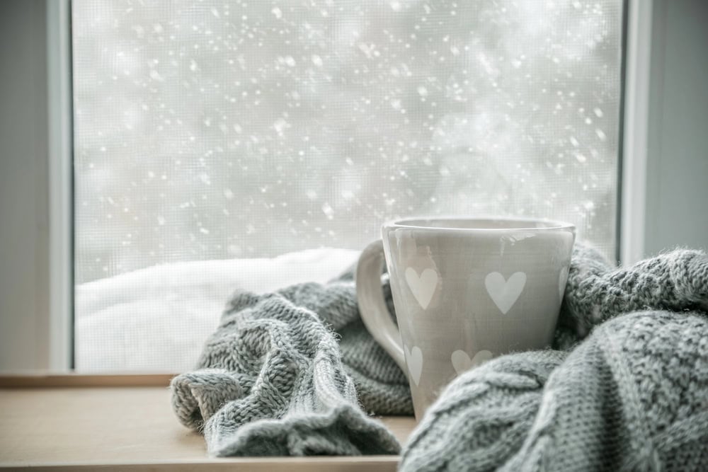 coffee mug with a knit blanket near a window